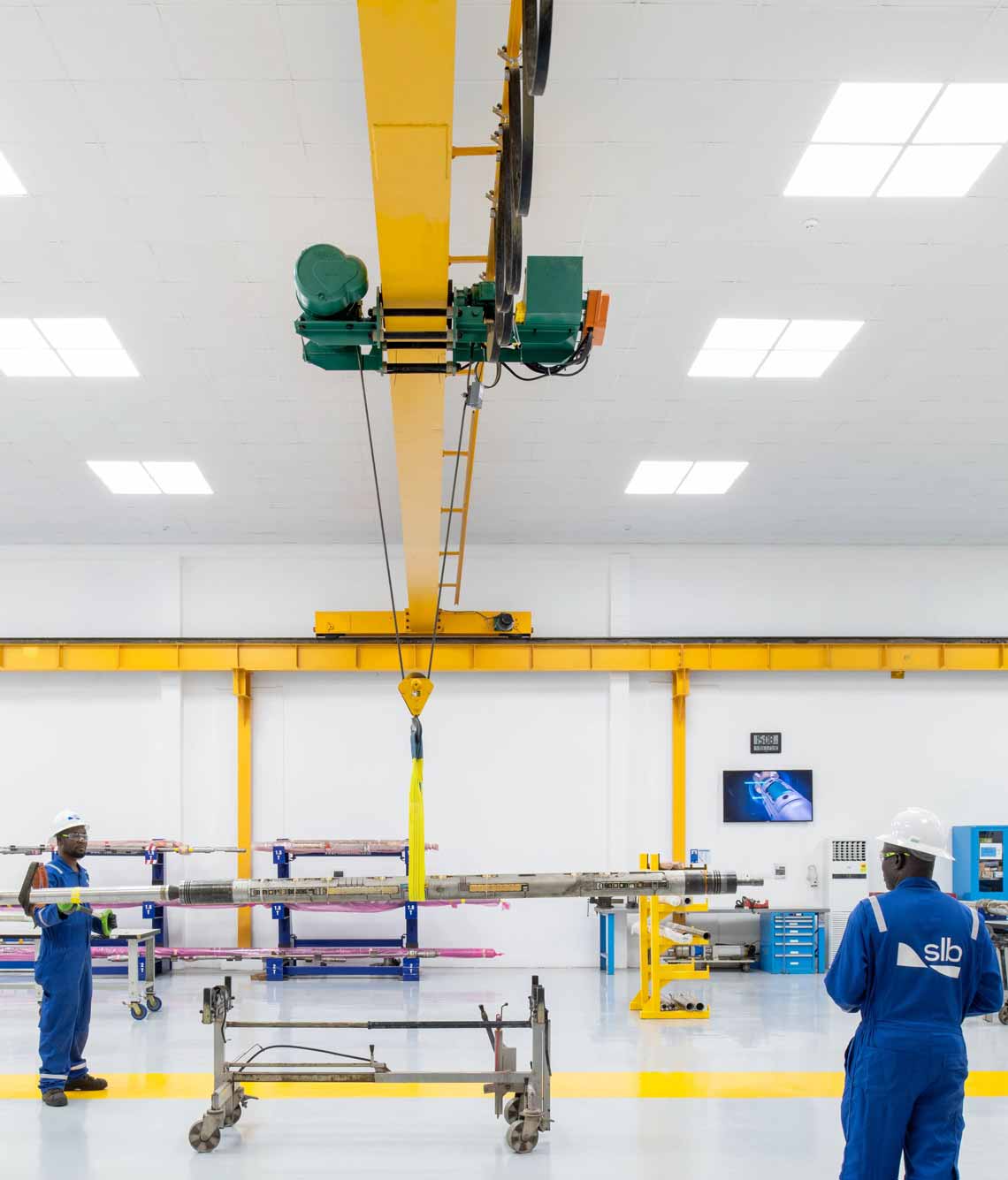 Two SLB operators wearing proper HSE equipment and using machinery to lift a heavy tool