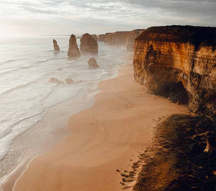 Scenic Australian coastal landscape with sandstone cliffs and sea stacks rising from the ocean at sunset.