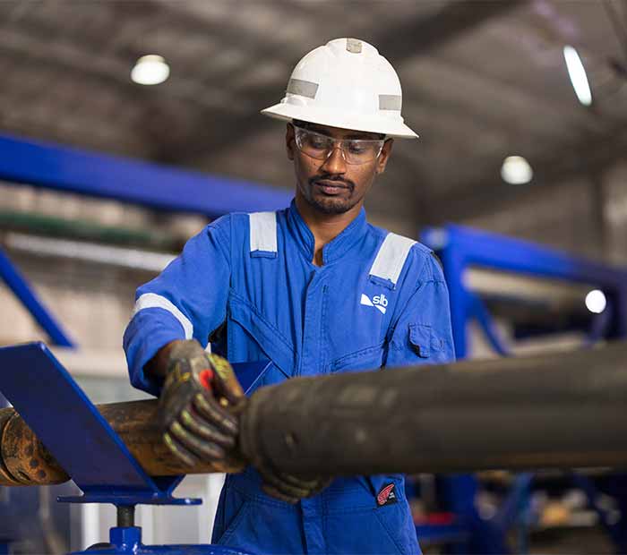 SLB field engineer in PPE operates downhole equipment in an industrial workshop, reflecting hands-on expertise and operational excellence.