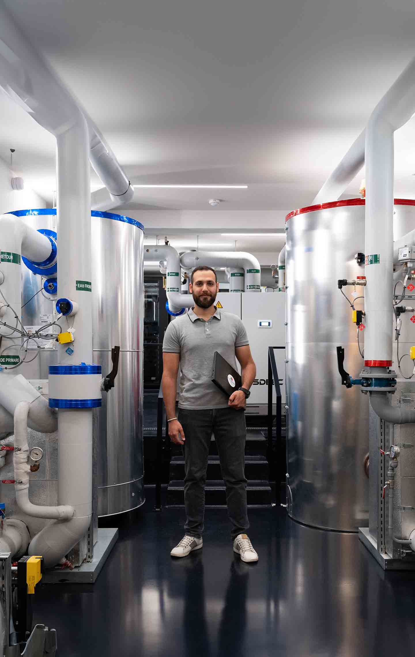 An employee standing in the Clamart facility with heat pump pipes on either side