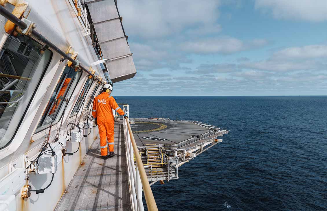 A SLB operator wearing orange coveralls on a platform rig overlooking the ocean