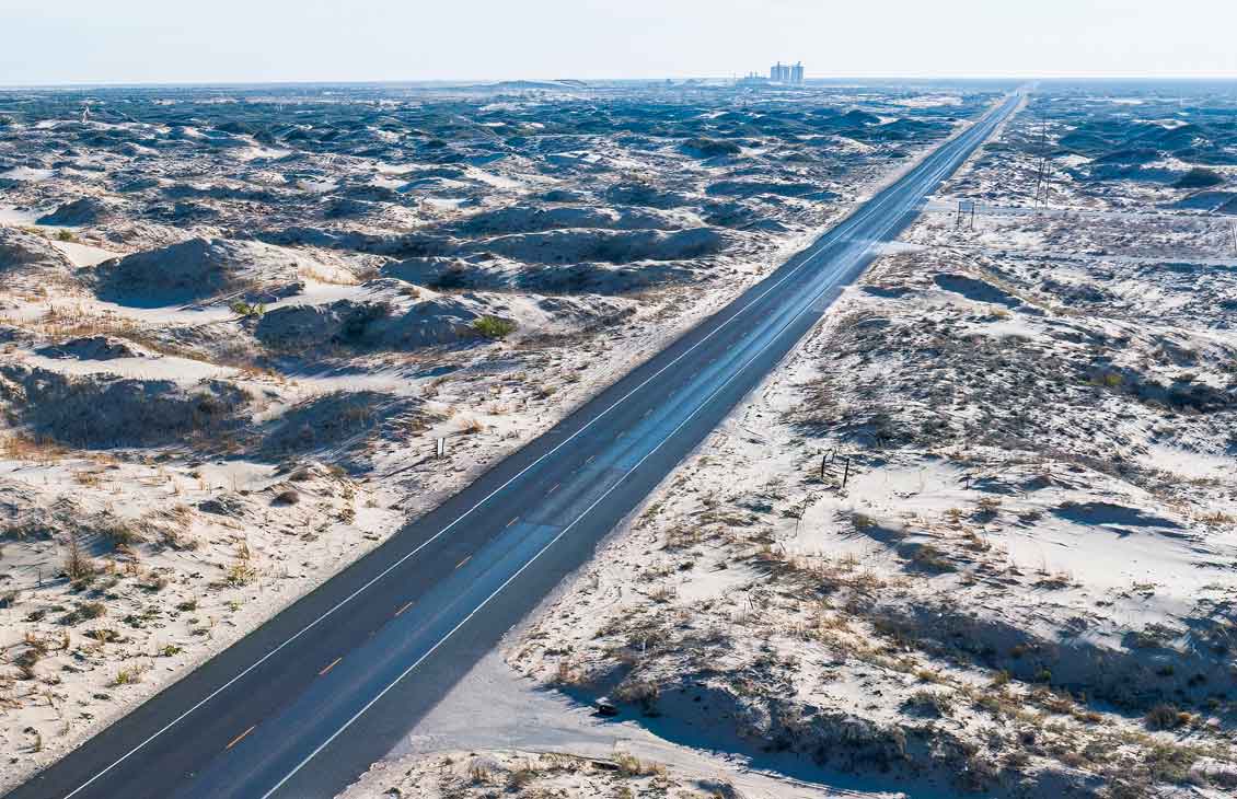 long straight road surrounded by sand dunes