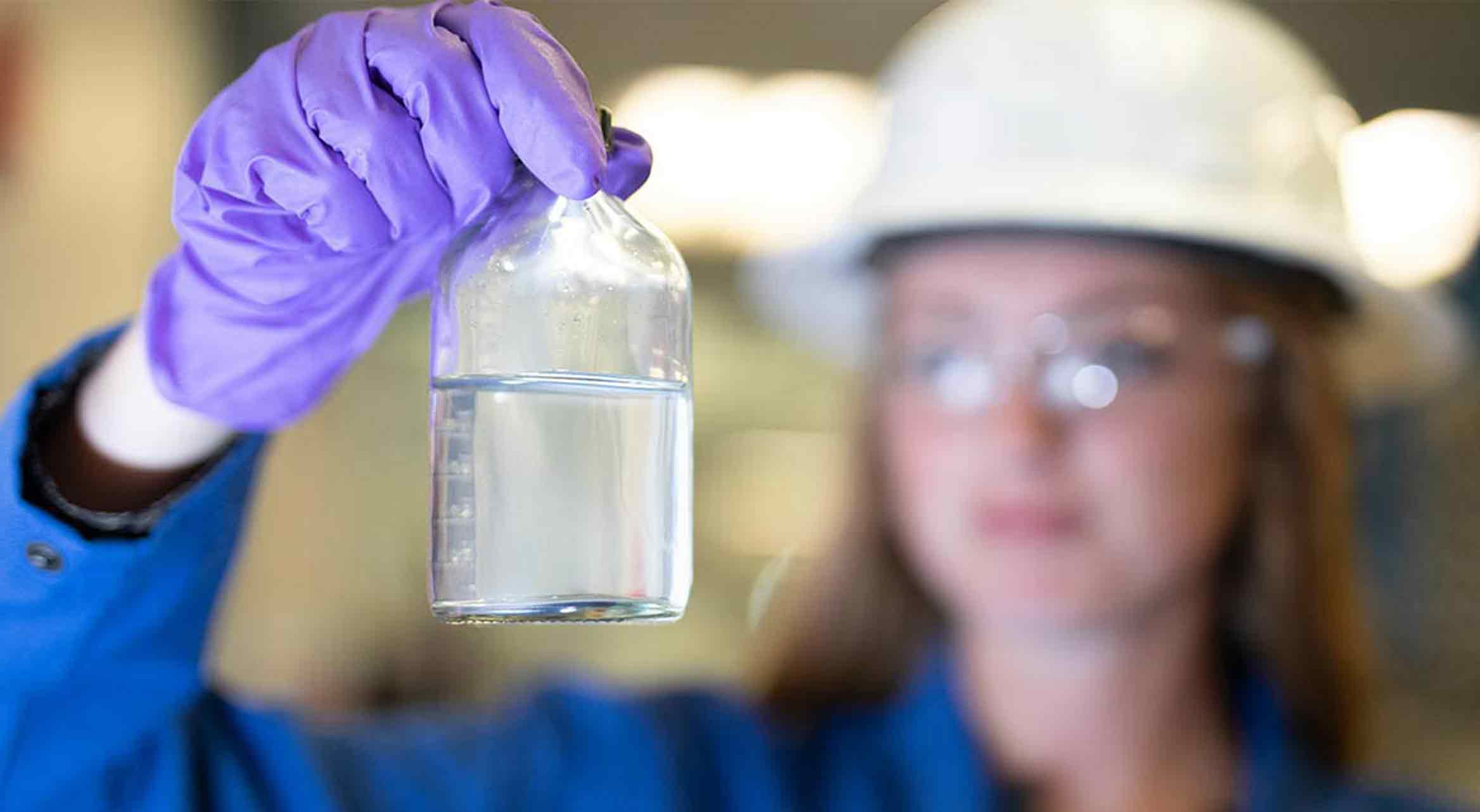 Technician holding bottle of clear water, showing impact of water clarifiers on produced water.